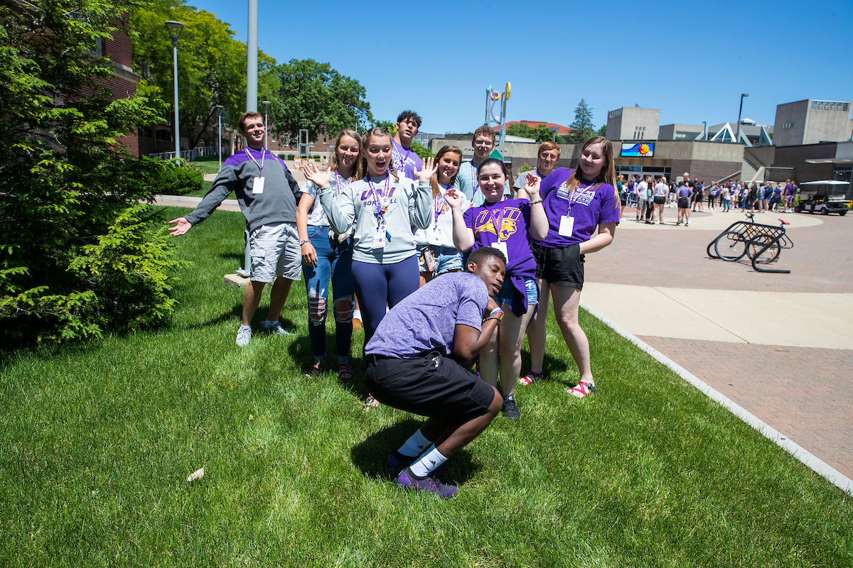 Group of students posing for a fun photo on the grass on a sunny summer day.