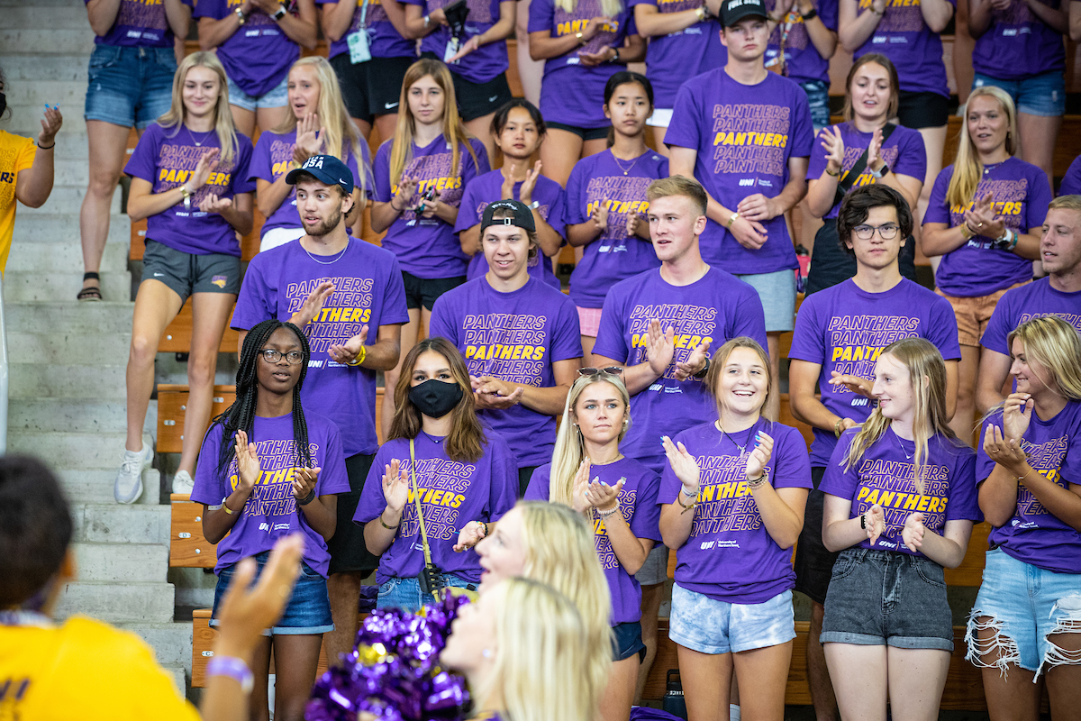 Students in a crowd clapping and smiling while wearing purple shirts with gold text that reads panthers.