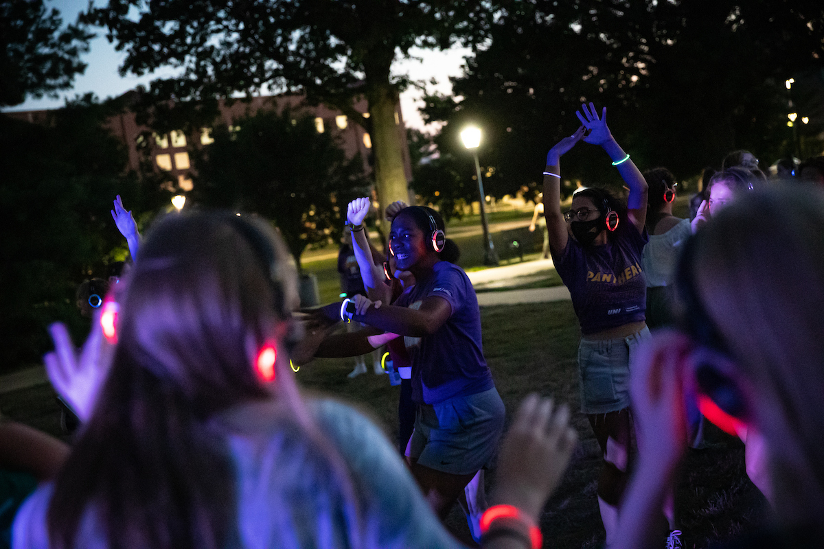 Students dancing outside on campus at sunset at a silent disco.