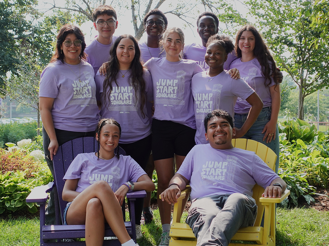 Group of 10 Jump Start Scholars Pathfinders and Leadership Team smiling together outside with sunshine and greenery behind them