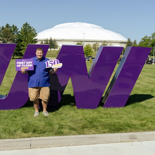 Student taking a picture in front of a big UNI sign on the first day of class.